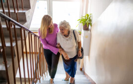 Young woman helps older woman to climb stairs in a residence.