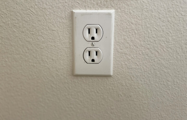 Slightly worn power outlet against an off-white wall.