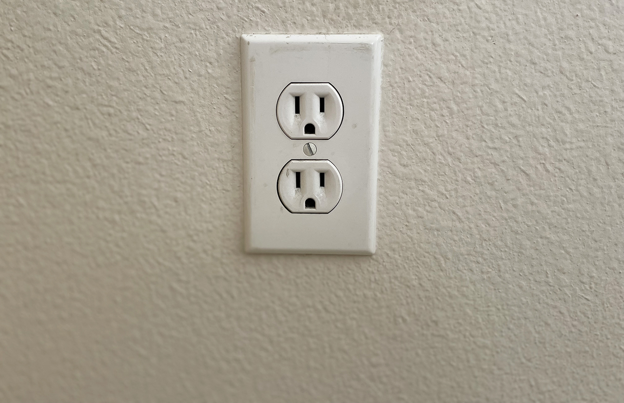 Slightly worn power outlet against an off-white wall.