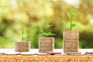 Three stacks of coins with little green sprouts growing out of the top of each coin stack. The stacks of coins get taller moving from left to right to imply growth.