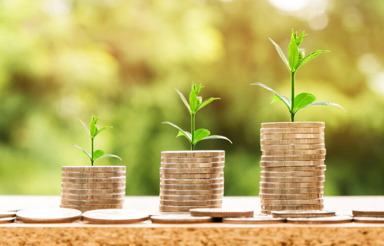 Three stacks of coins with little green sprouts growing out of the top of each coin stack. The stacks of coins get taller moving from left to right to imply growth.